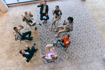 Top view of a diverse group of young business entrepreneurs gathered in a circle for a meeting, discussing corporate challenges and innovative solutions within the modern confines of a large