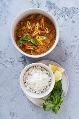 Red curry chicken with white rice in bowl on grey background