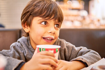 Child with hot milk moustache drinking from a paper cup at a coffee shop