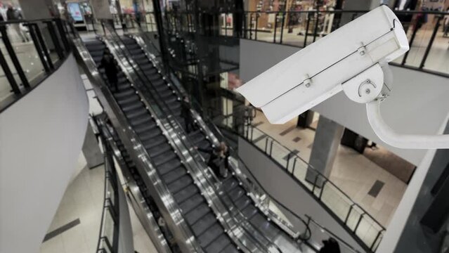 CCTV camera in a crowded public place in a shopping center. Security video surveillance camera with blurred background installed near the escalator in an airport or train station. 4k footage
