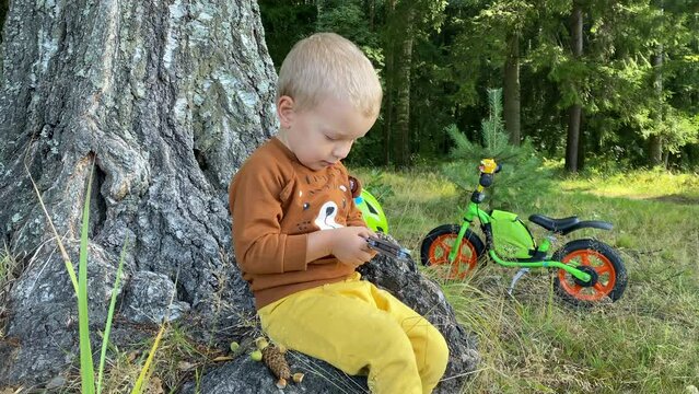 toddler child playing with multitool in summer forest, little boy with balance bike in park