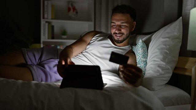 Young arab man shopping with laptop and credit card sitting on bed at bedroom