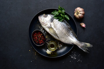 Dorado fish with ingridients for making on black plate . Top view with copy space.