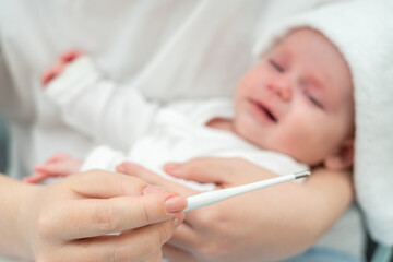Mother calms crying baby while checking fever. Concept of sick baby