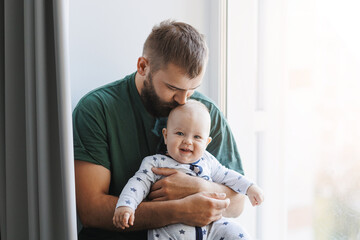 Father hugs baby boy, young man kisses his son on head in living room. Concept lifestyle parenting...
