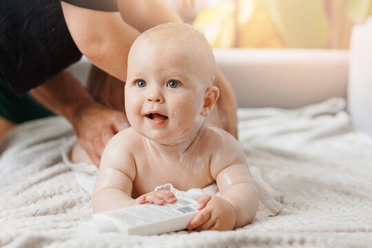 Mother applying body cream on her little happy baby son at home. Concept lotion for skin of infant