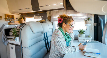 One solo traveler woman enjoy time and indoor leisure activity inside a modern camper van motorhome using mobile phone and roaming wireless connection. Modern people and technology on travel