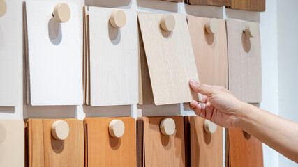 Designer hand picking wood samples board from material swatch wall display in material library. Choosing wooden laminate texture in beige tone collection for interior architecture or furniture design