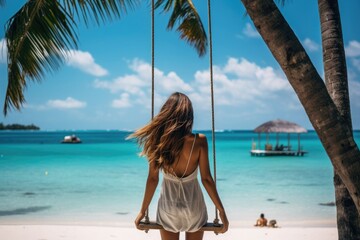 Rear view of a young woman sitting on a swing with sea view in the background. Inspiring tropical landscape