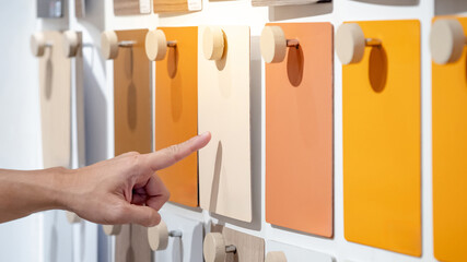 Designer hand pointing at colorful laminate sheet on material swatch wall display in material library. Choosing color board from collection for interior architecture and furniture finishing design - obrazy, fototapety, plakaty