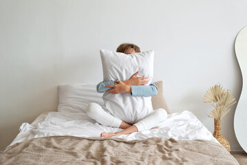 Time to sleep, sleep deficiency, good morning concept. Teenager boy sitting on bed, embracing white...