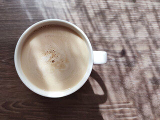 cup of coffee on a wooden table with shadows in the sunlight, top view