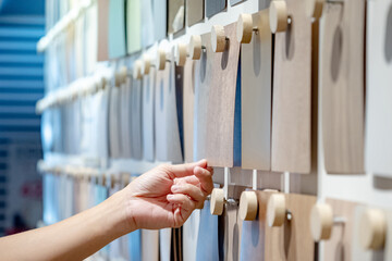 Designer hand picking wood samples board from material swatch wall display in material library. Choosing wooden laminate texture in beige tone collection for interior architecture or furniture design