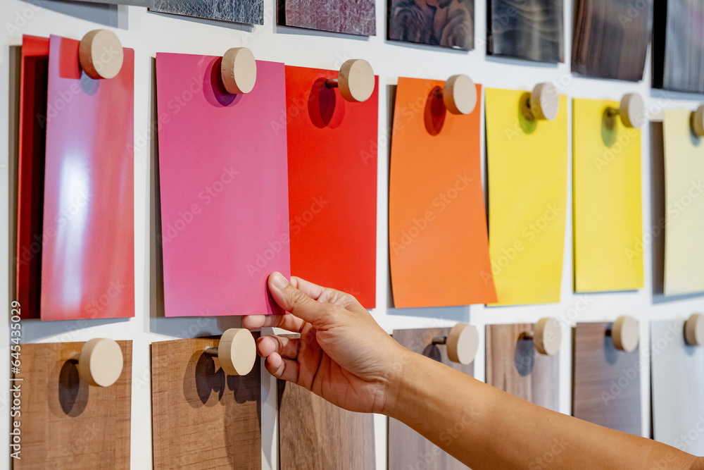 Wall mural designer hand picking colorful laminate sheet on material swatch wall display in material library. c