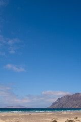 Obraz premium White sand beach. Famara beach. Turquoise water, island of La Graciosa and cliffs in the background. Sky with big white clouds. Caleta de Famara.Lanzarote, Canary Islands, Spain.