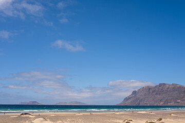 White sand beach. Famara beach. Turquoise water, island of La Graciosa and cliffs in the background. Sky with big white clouds. Caleta de Famara.Lanzarote, Canary Islands, Spain.