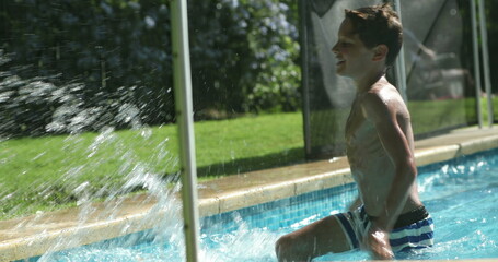 Boy at swimming pool water splashing water outside pool. Child splashes water with hand