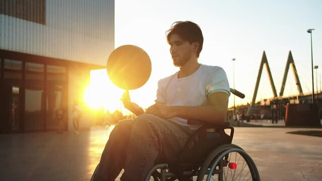 A man in a wheelchair spinning a basketball at sunset