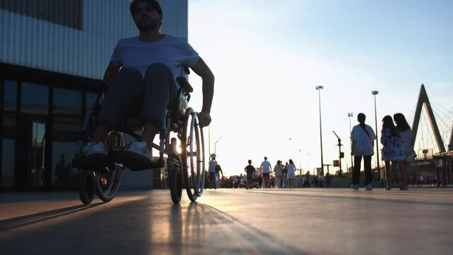 A man in a wheelchair riding on the crowded street at sunset