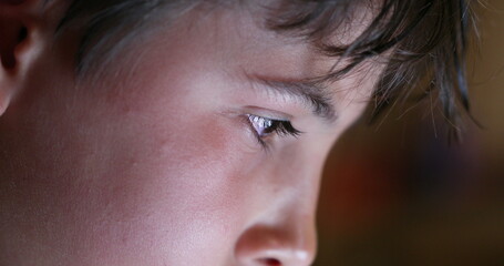 Boy eyes looking at device screen. Child staring at bright blue display closeup face