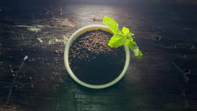 Black Tea Powder ( chai patti) with mint leaves felling to white bowl on wooden Background , top view 4K Footage,