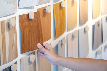 Designer hand picking wood samples board from material swatch wall display in material library. Choosing wooden laminate texture in brown tone collection for interior architecture or furniture design