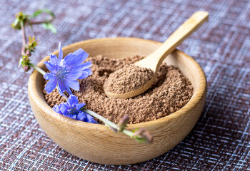 Ground chicory root in a wooden cup and chicory flowers on a rustic wooden background. Alternative medicine. Healthy drinks. chicory drink - obrazy, fototapety, plakaty