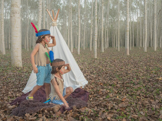 Twins playing at being Native Americans next to a tepee and with their hand on their foreheads to...