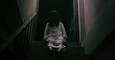 Obraz na płótnie Canvas Horror scene of a mysterious Scary Asian ghost woman creepy have hair covering the face sitting on staircase at abandoned house with background dark scene movie at night, festival Halloween concept