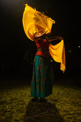 a traditional Indonesian dancer dances with a yellow scarf that floats in the air