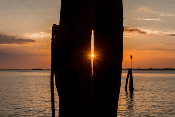 Il sole sorge sulla laguna di Venezia e la luce passa attraverso lo spazio fra due pali di legno