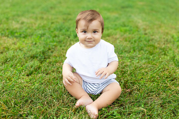 A baby sits on green lawn, freedom of movement for the child. Summer time, happy baby.