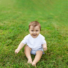 A baby sits on green lawn, freedom of movement for the child. Summer time, happy baby.