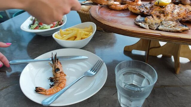 Close-up of female putting freshly cooked grilled shrimps on a plate at cafe or restaurant