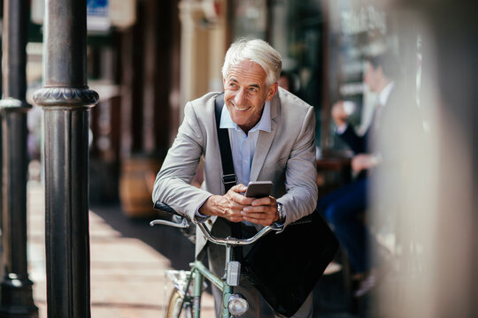 Senior businessman using his smartphone while commuting to work with a bicycle in the city - Powered by Adobe