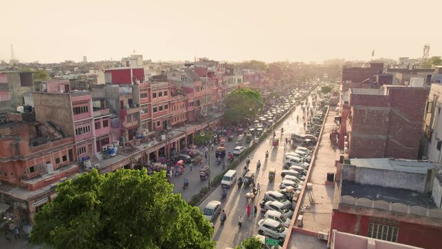 A drone moving aerial shot of a Urban suburb locality with vehicles or traffic passing in a busy Indian city market or traditional old bazaar and people walking on the street in a daylight.
