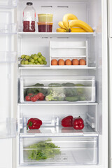 Fridge open with food inside. Eggs and fresh vegetables.