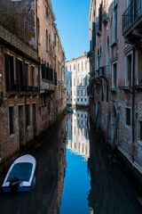 Fototapeta na wymiar Una piccola barca ormeggiata in un canale di Venezia in una giornata di sole con i palazzi che si riflettono nell'acqua