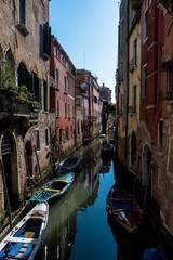 Alcune piccole barche ormeggiate in un canale di Venezia in una giornata di sole con i palazzi che si riflettono nell'acqua
