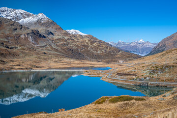 Mountains and blue sky are reflected in the calm waters of Lej Nair ("Black Lake") near the summit of the Bernina Pass in Switzerland