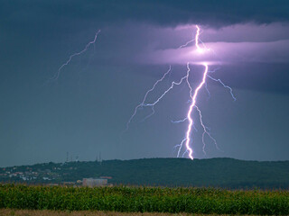 Branched lightning hits earth behind a hill