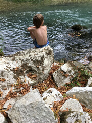 dreaming boy sitting on a rock near the mountain river in the national park. huge white rocks with moss and fallen leaves around