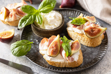Toast or bruschetta with bacon and figs, cream cheese and honey on a gray stone background. Italian appetizer recipe.