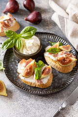 Toast or bruschetta with bacon and figs, cream cheese and honey on a gray stone background. Italian appetizer recipe. Copy space.