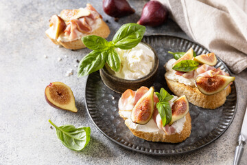 Italian appetizer recipe. Toast or bruschetta with bacon and figs, cream cheese and honey on a gray stone background. Copy space.