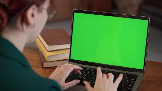 Girl Typing on Keyboard Of Laptop with Green Mock-up Screen. Female Student Learning Online in Cozy Room- Library