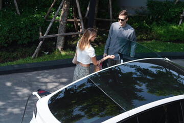 Young couple travel with EV electric car charging in green sustainable city outdoor garden in...