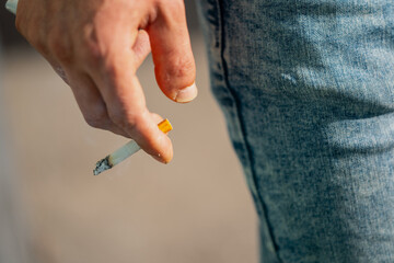 Man holding a burning cigarette in hand close up during summer while wearing jeans