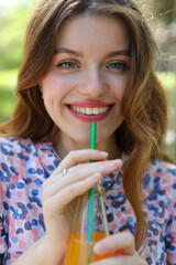 A young woman exudes elegance and happiness while enjoying a healthy juice outdoors during a summer vacation.