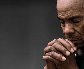 man praying to god with hands together Caribbean man praying with grey background stock image stock photo	